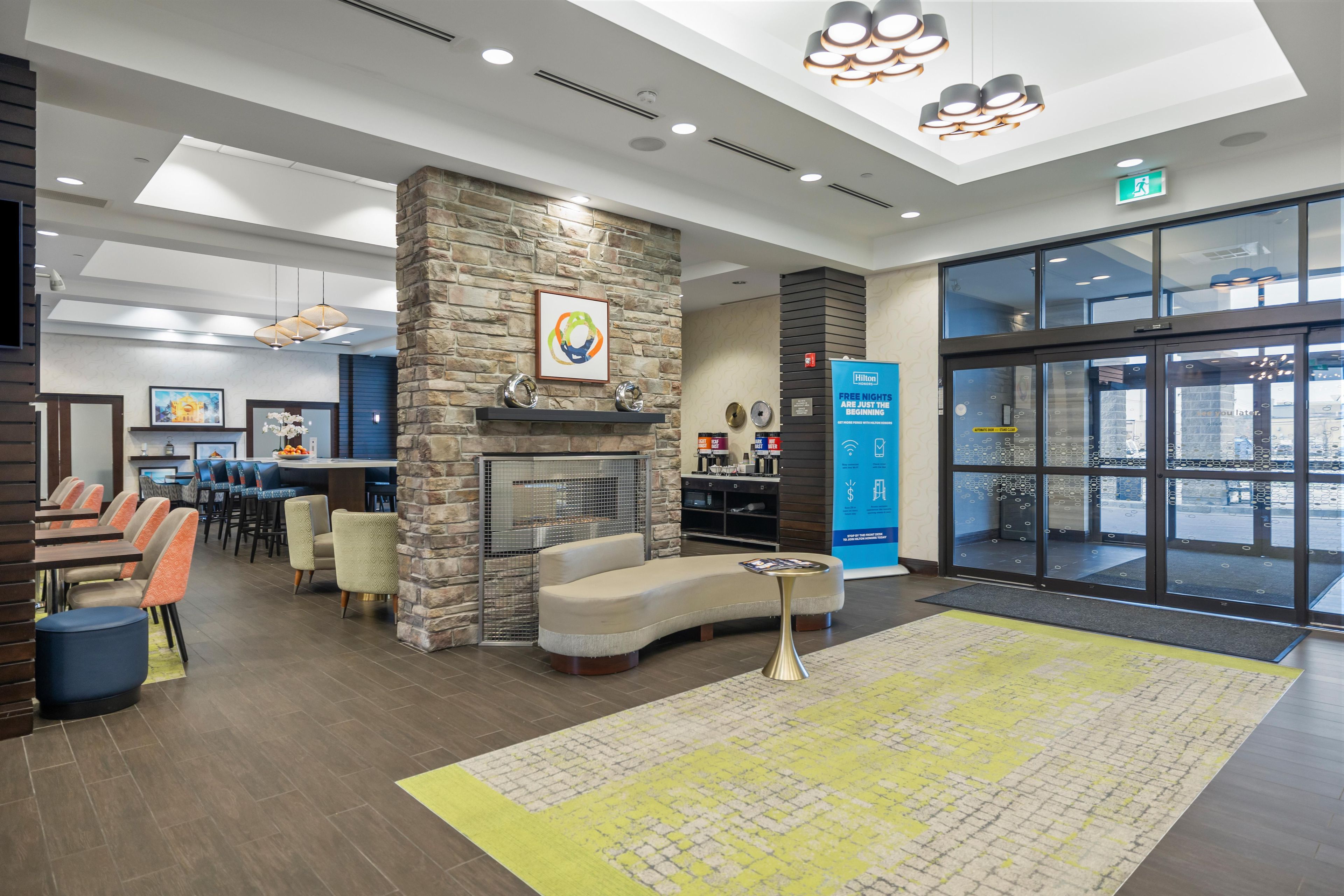 A hotel lobby with a stone fireplace, seating area, and a large glass door entrance.