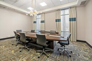 A conference room with a long table, chairs, a chandelier, and large windows with curtains.