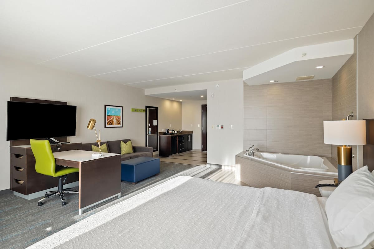 Ein modernes Hotelzimmer mit Bett, Schreibtisch, Stuhl, Fernseher, Küchenzeile und Badewanne.