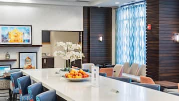 Un moderno vestíbulo de hotel con una isla central, asientos de bar e iluminación decorativa.
