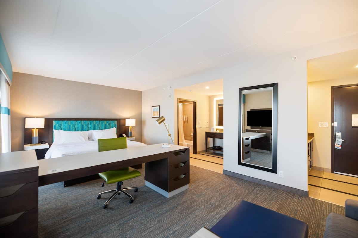 Ein Hotelzimmer mit Bett, Schreibtisch, Stuhl, Lampe und Fernseher.