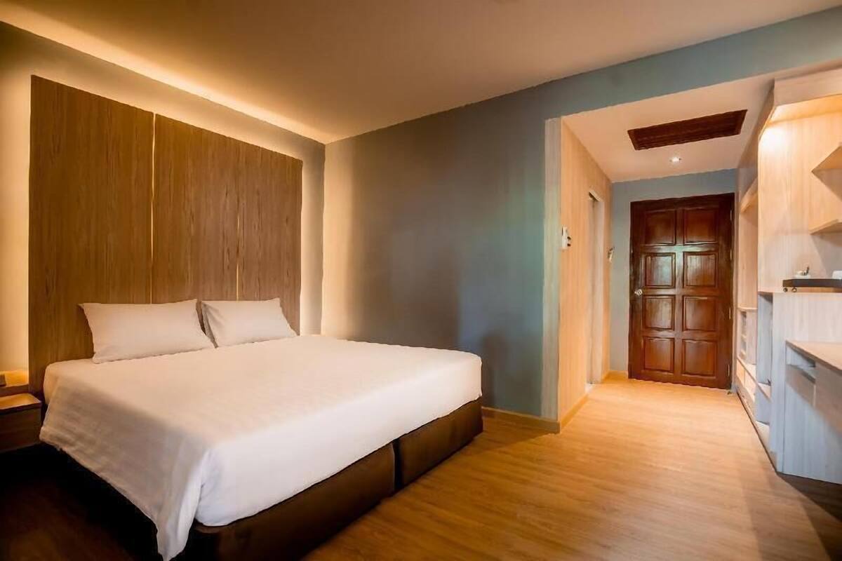 A bedroom with a large bed, wooden headboard, a wooden wardrobe, and a door leading to another room.