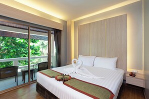 Habitación de hotel con una cama grande, un balcón con sillas de mimbre y vistas al verdor.