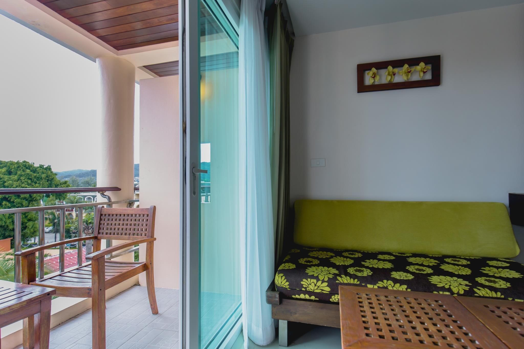 A balcony with a wooden chair, a small table, and a sofa with a floral cushion.