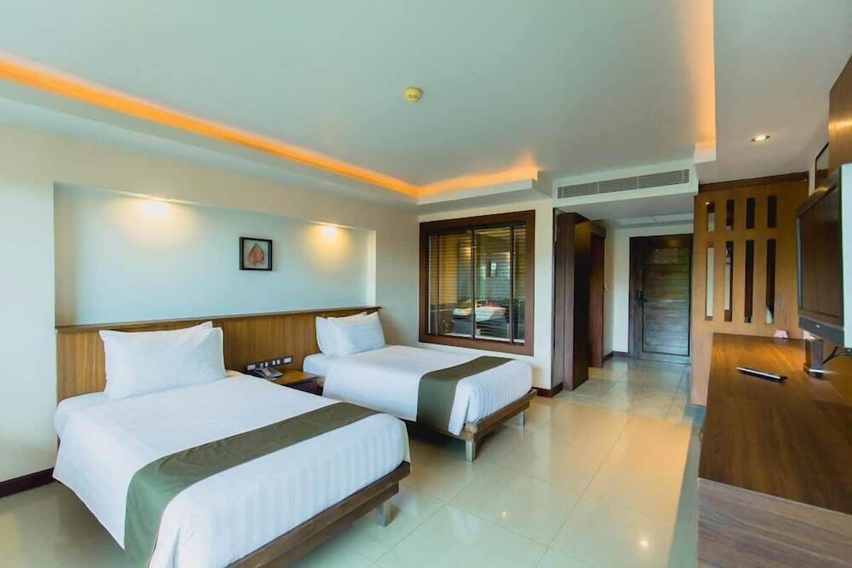 A hotel room with two beds, a TV, a desk, and a window with blinds.