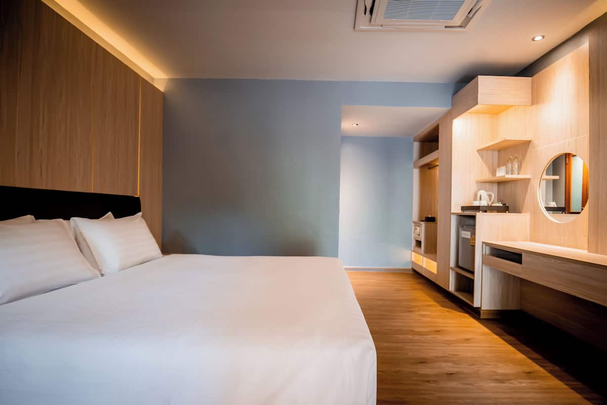 A modern hotel room with a large bed, wooden paneling, a built-in desk, and a mirror.