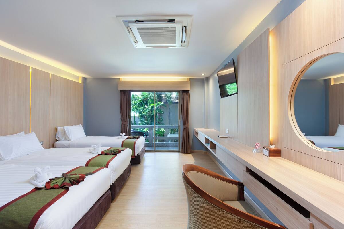 A hotel room with two beds, a large mirror, a TV, and a balcony with a view of greenery.