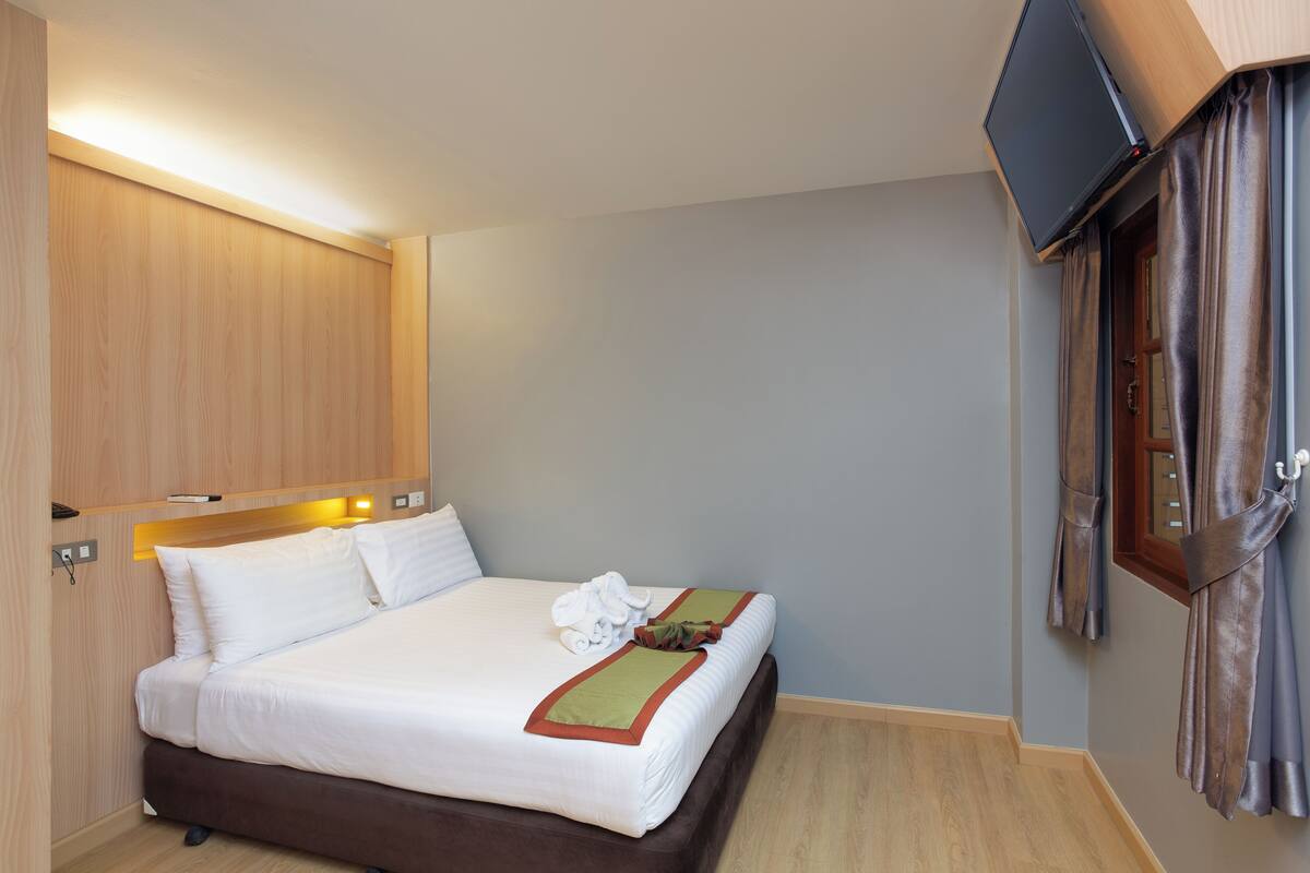 A hotel room with a bed, a flat-screen TV mounted on the wall, and a wooden wardrobe.