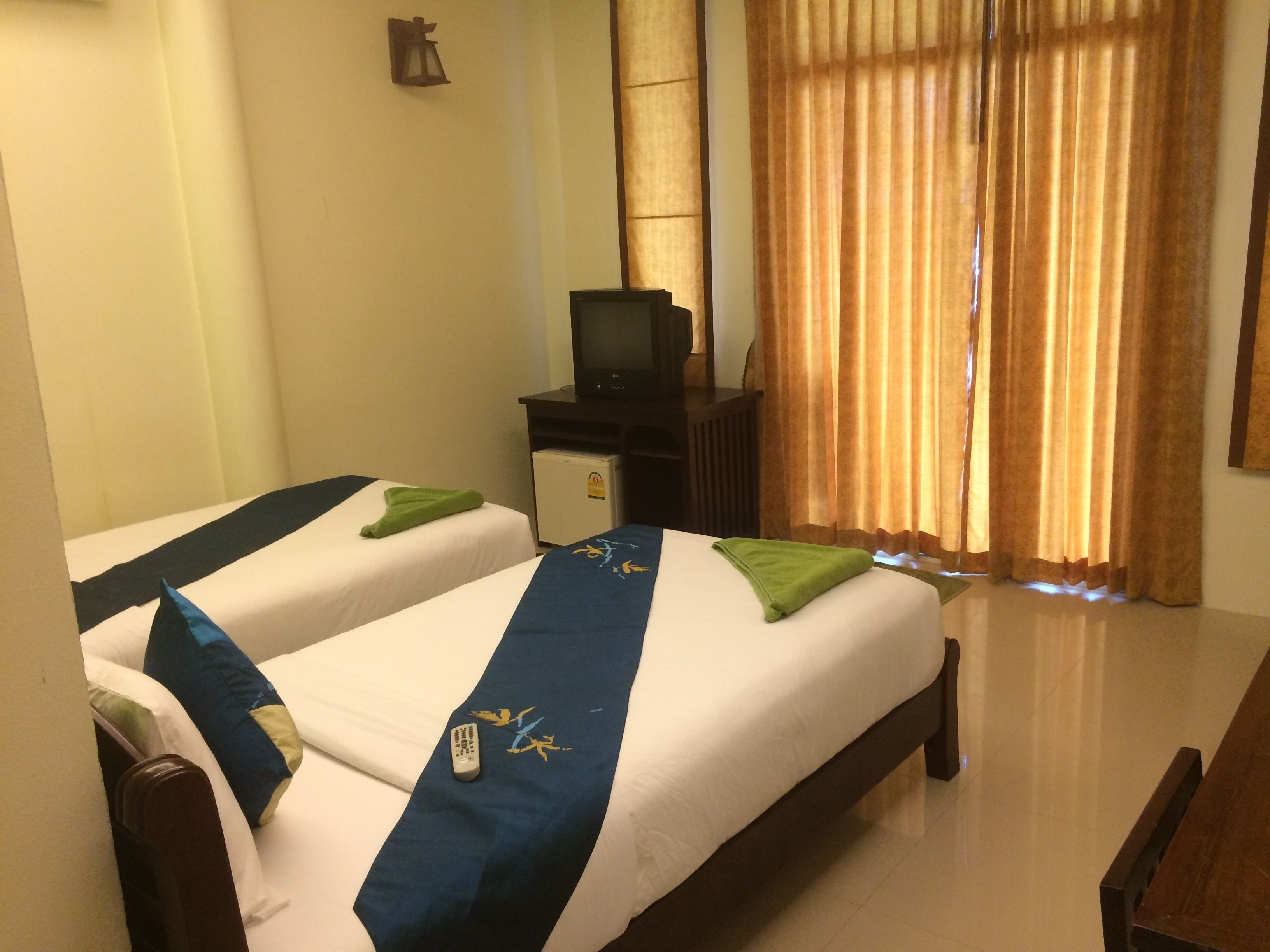 A hotel room with two beds, a television on a small table, and a window with curtains.