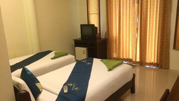 A hotel room with two beds, a television on a small table, and a window with curtains.