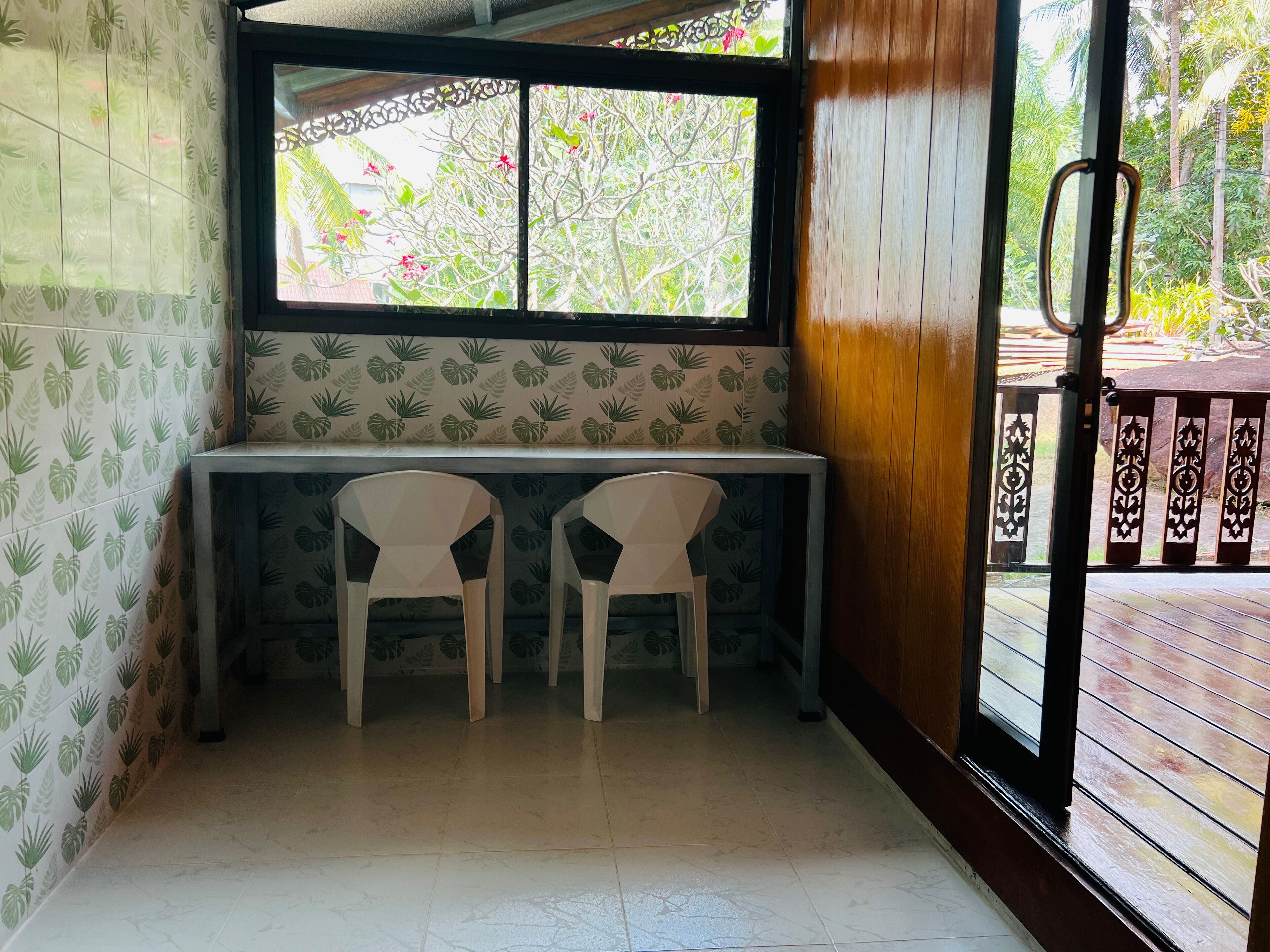 A small room with a window, two white chairs, a table, and patterned wallpaper.