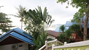 Un barrio residencial con una escalera que lleva a una casa con techo azul, rodeada de vegetación exuberante y vista al mar.