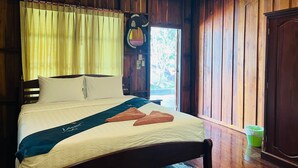 Una habitación con paneles de madera, una cama, una ventana con cortinas y un bote de basura verde.