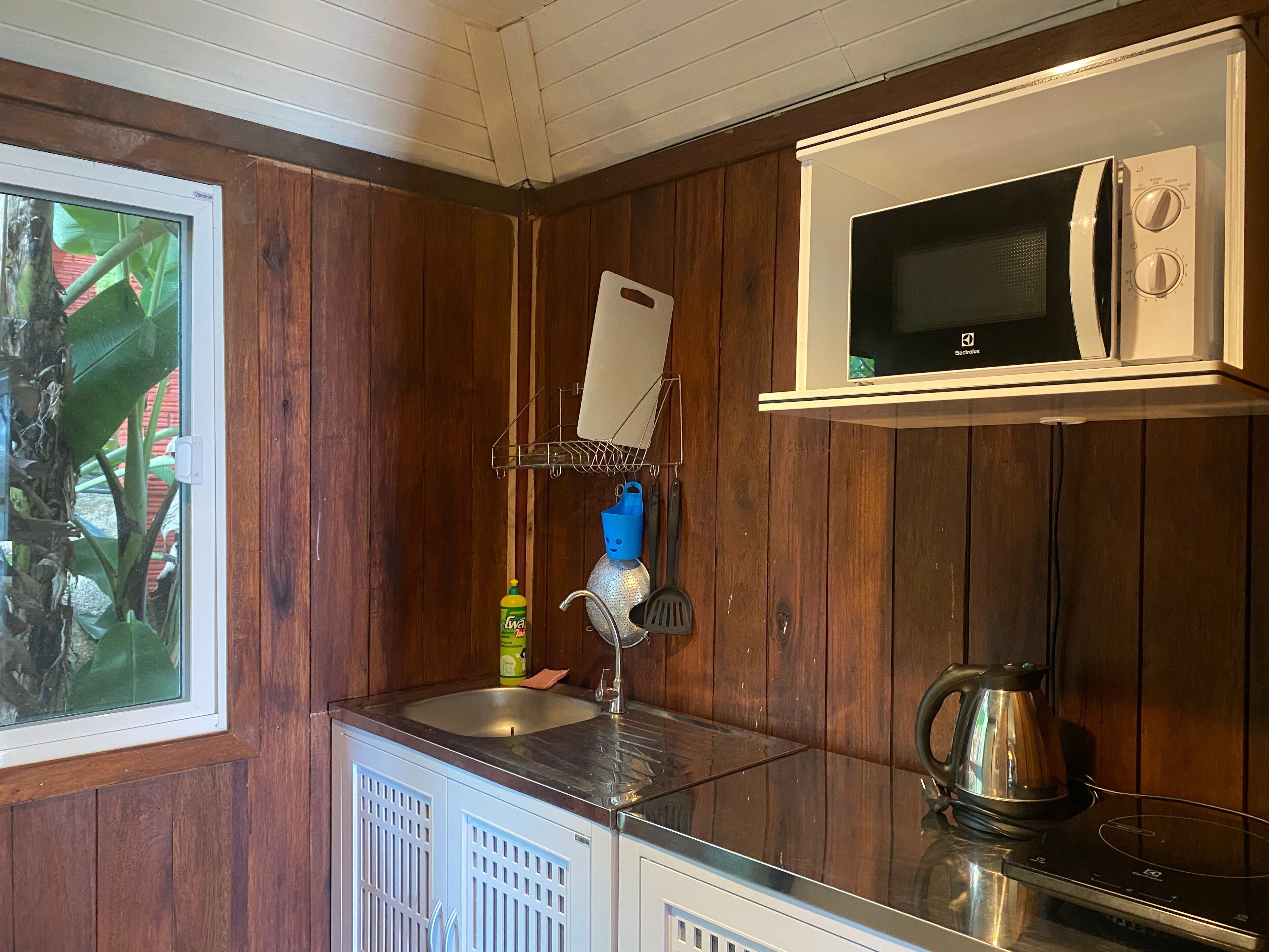 Una cocina compacta con microondas, lavamanos y hervidor.
