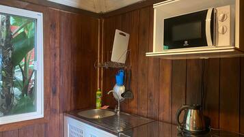 Una cocina compacta con microondas, lavamanos y hervidor.