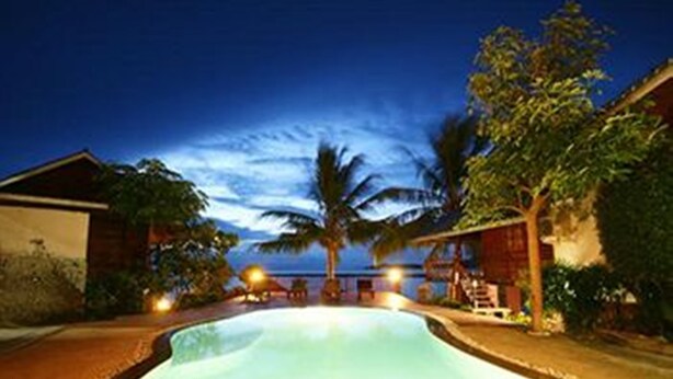 Una piscina al anochecer con vista al océano y palmeras.