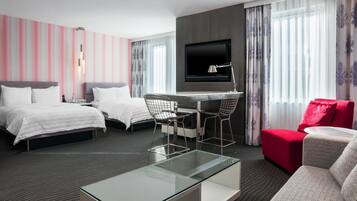 A hotel room with two beds, a desk with chairs, a TV, and a glass coffee table.