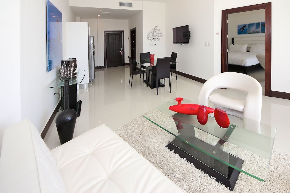 A modern living room with a glass coffee table, white sofa, and a dining area with a glass table and chairs.