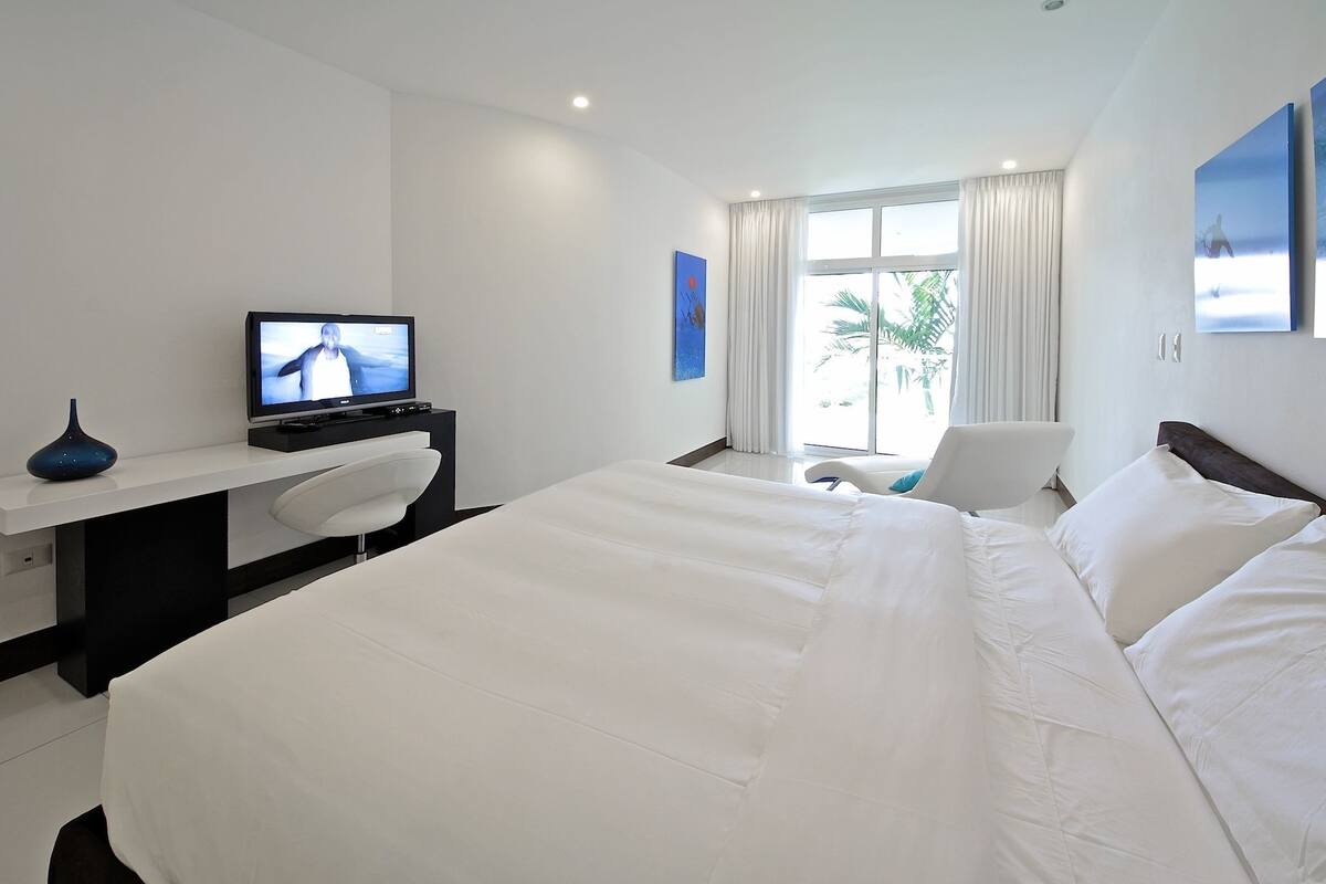 A hotel room with a large bed, a desk with a computer, a chair, and a television.