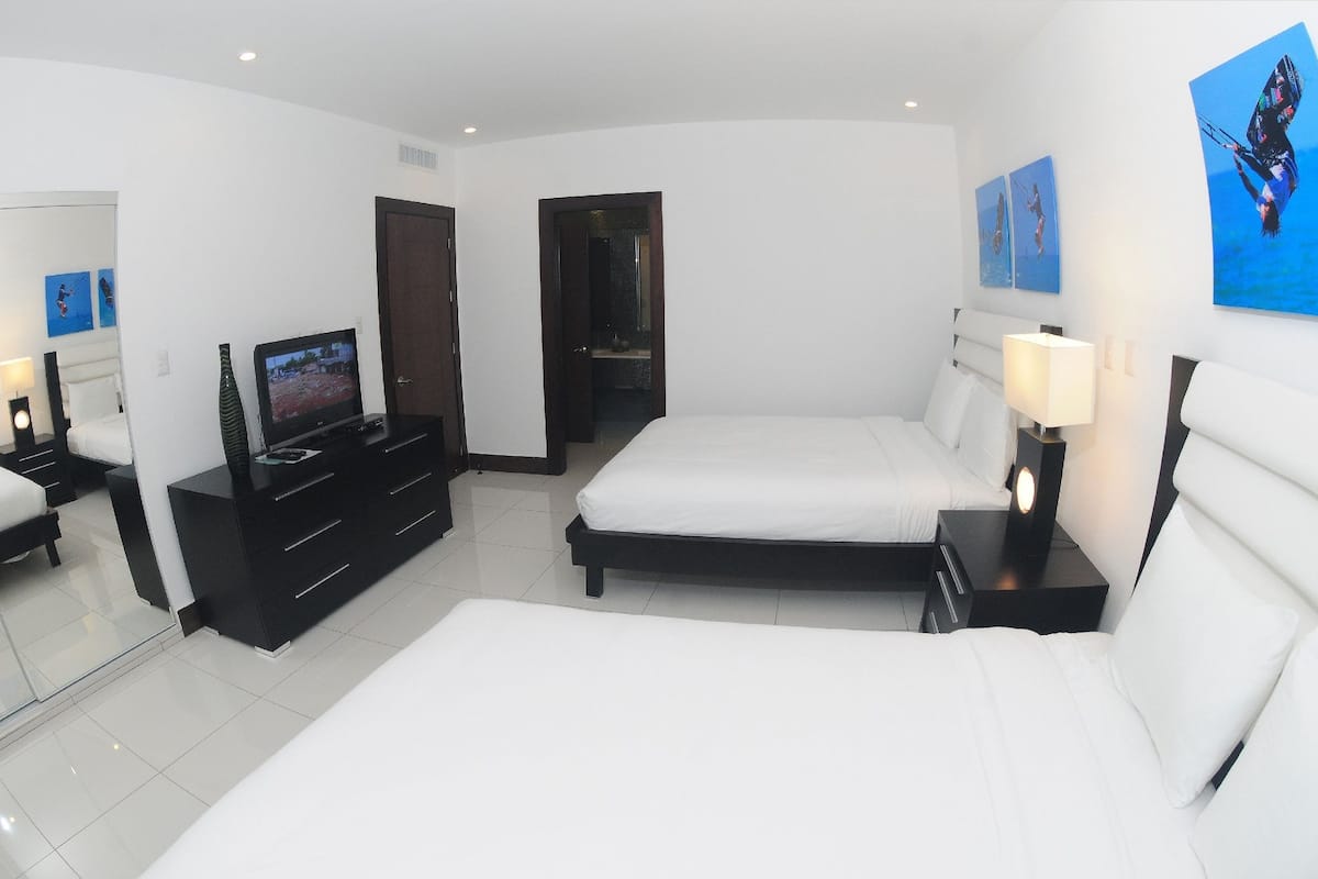 A modern hotel room with two beds, a TV, a dresser, and artwork on the walls.
