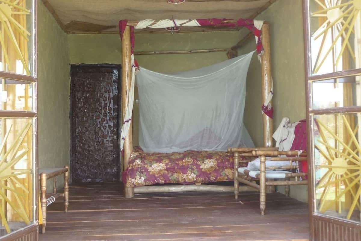 Une pièce avec un lit recouvert d’une moustiquaire, une chaise en bois et une porte ornée d’un rideau à motifs.