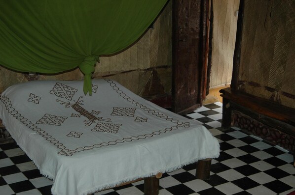 A bed with a white bedspread featuring a geometric pattern, a green canopy, and a checkered floor.