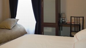 A hotel room with two beds, a desk with a chair, a lamp, and a window with curtains. - Hôtel Bel Air (Paris)