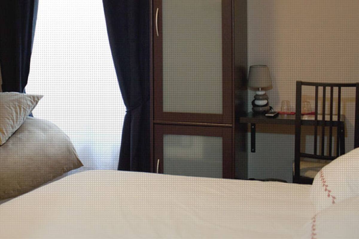 Een hotelkamer met twee bedden, een bureau met stoel, een lamp en een raam met gordijnen.