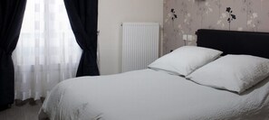 A bed with white bedding in a room with floral wallpaper and a radiator. - Hôtel Bel Air (Paris)