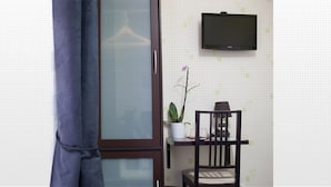 A room with a sliding door, a small table with a chair, a potted plant, and a mounted TV. - Hôtel Bel Air (Paris)