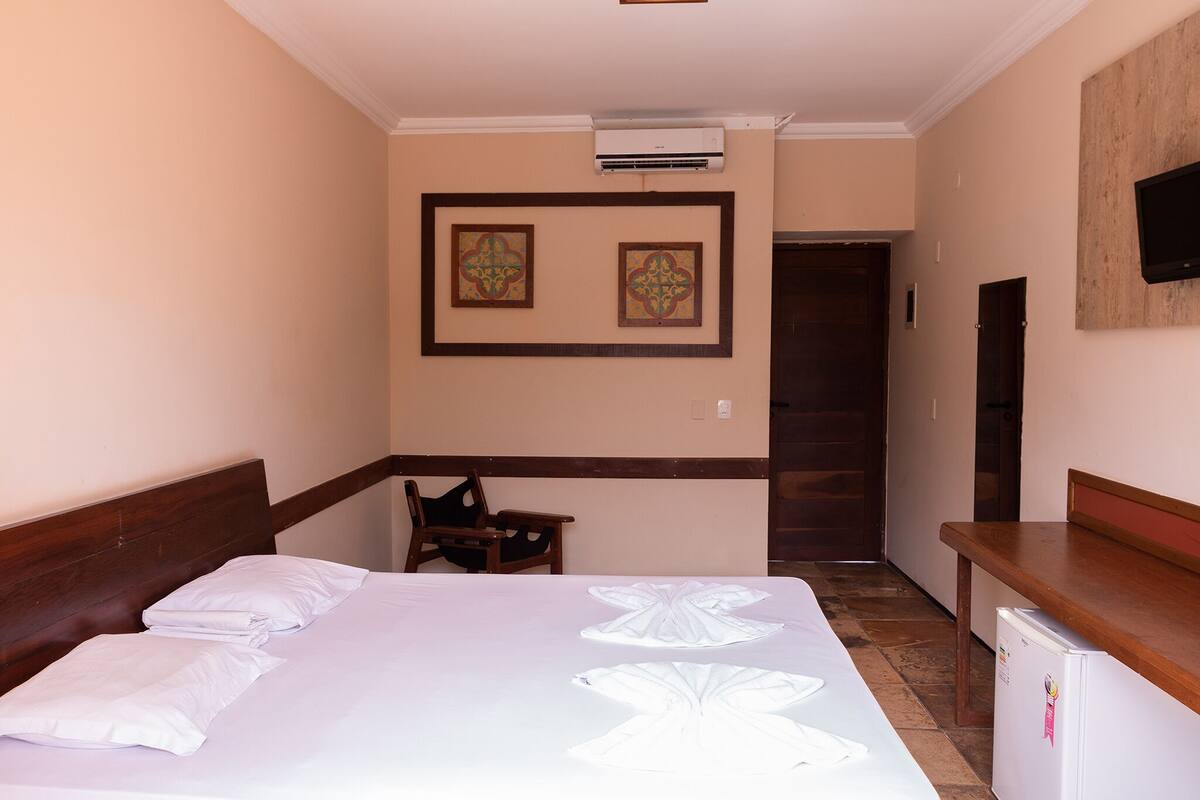 Habitació d'hotel amb un llit, un reposacapses de fusta, una taula petita i un televisor fixat a la paret.