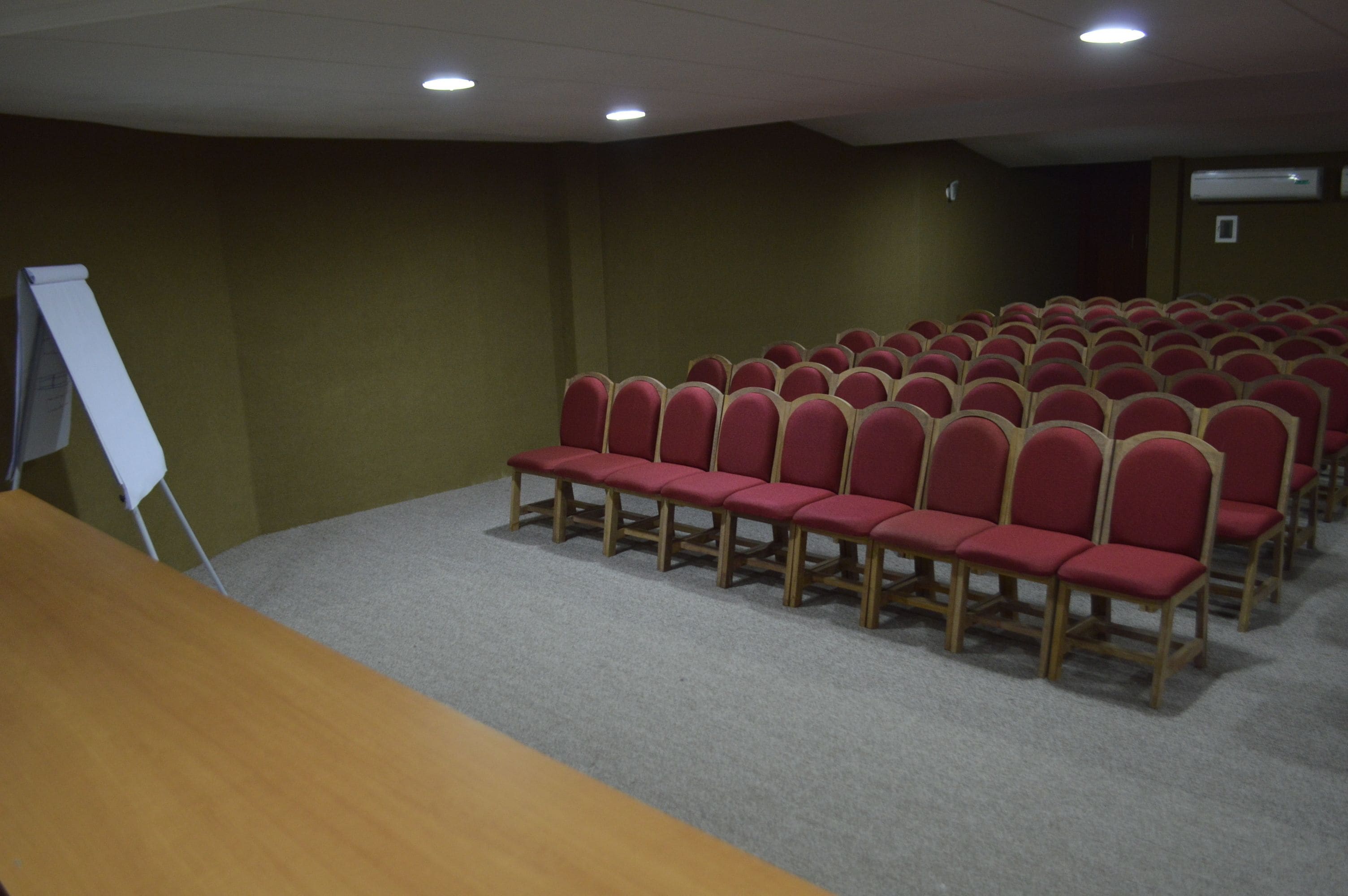 A conference room with rows of red chairs, a whiteboard, and carpeted flooring.