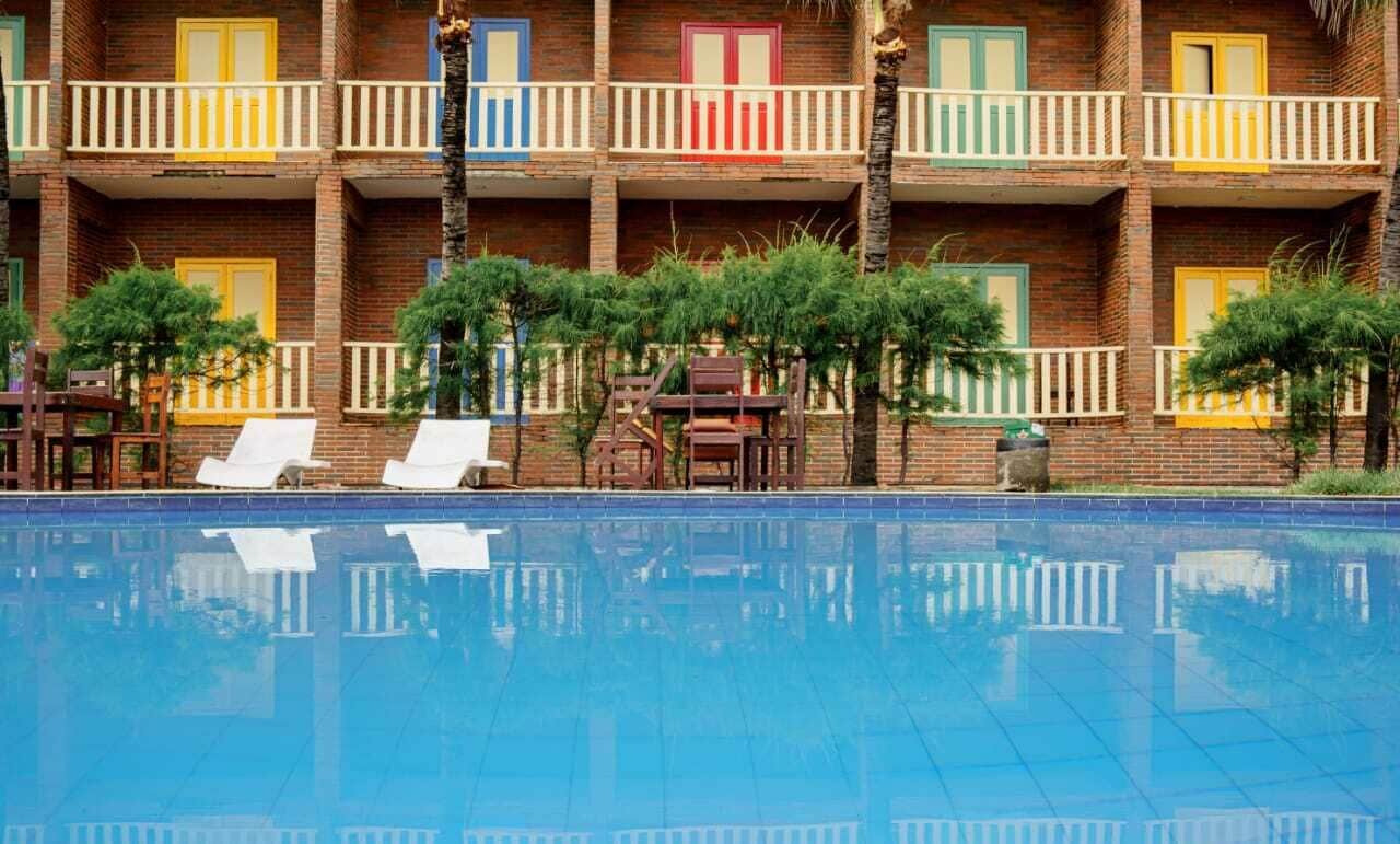 A hotel with a swimming pool, multiple balconies with colorful railings, and outdoor seating.