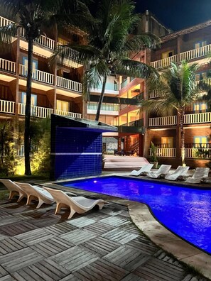 Un espace piscine d’hôtel avec des chaises longues et une piscine dont le fond est recouvert de carreaux bleus.