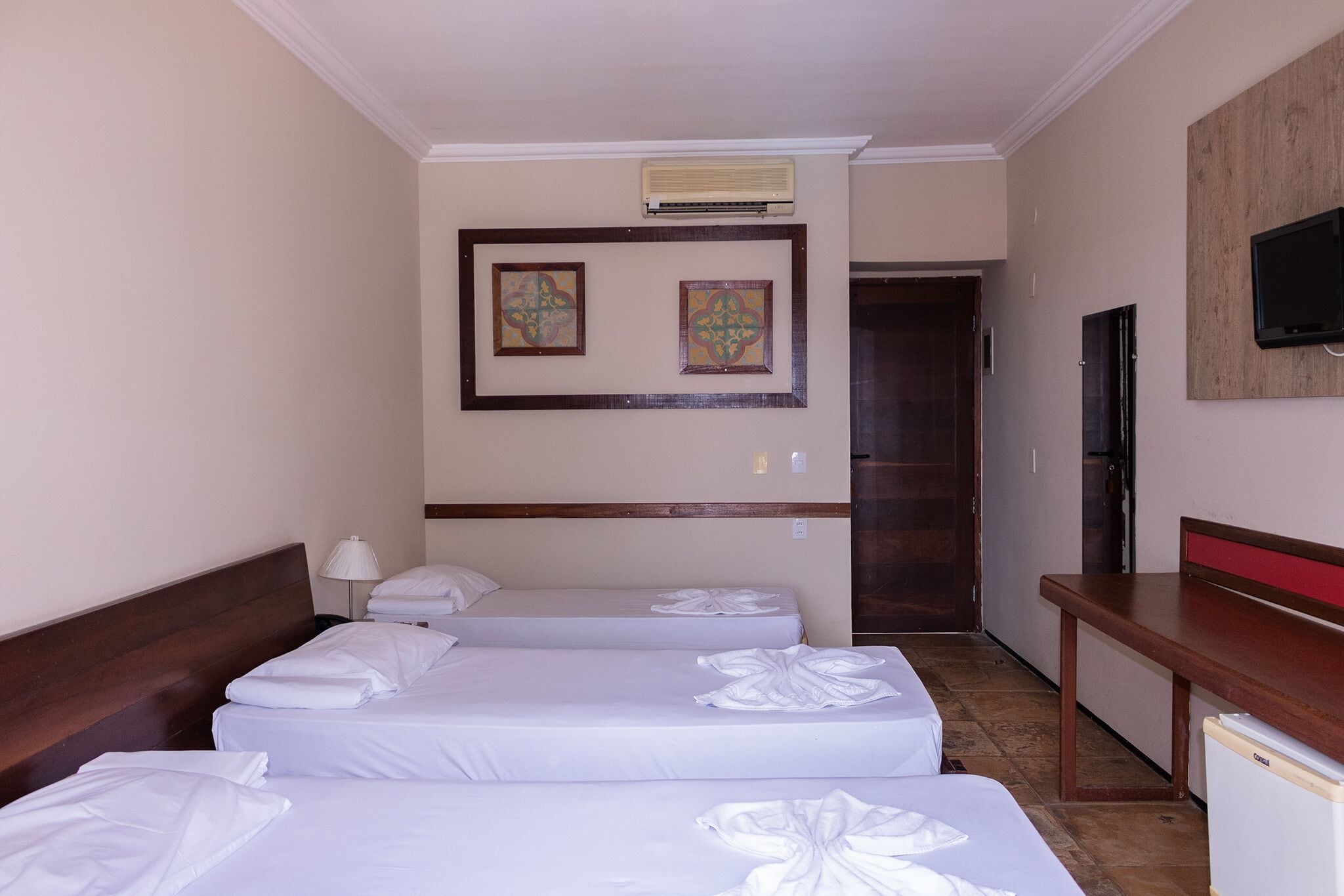 A hotel room with two beds, a desk, a TV, and a refrigerator.