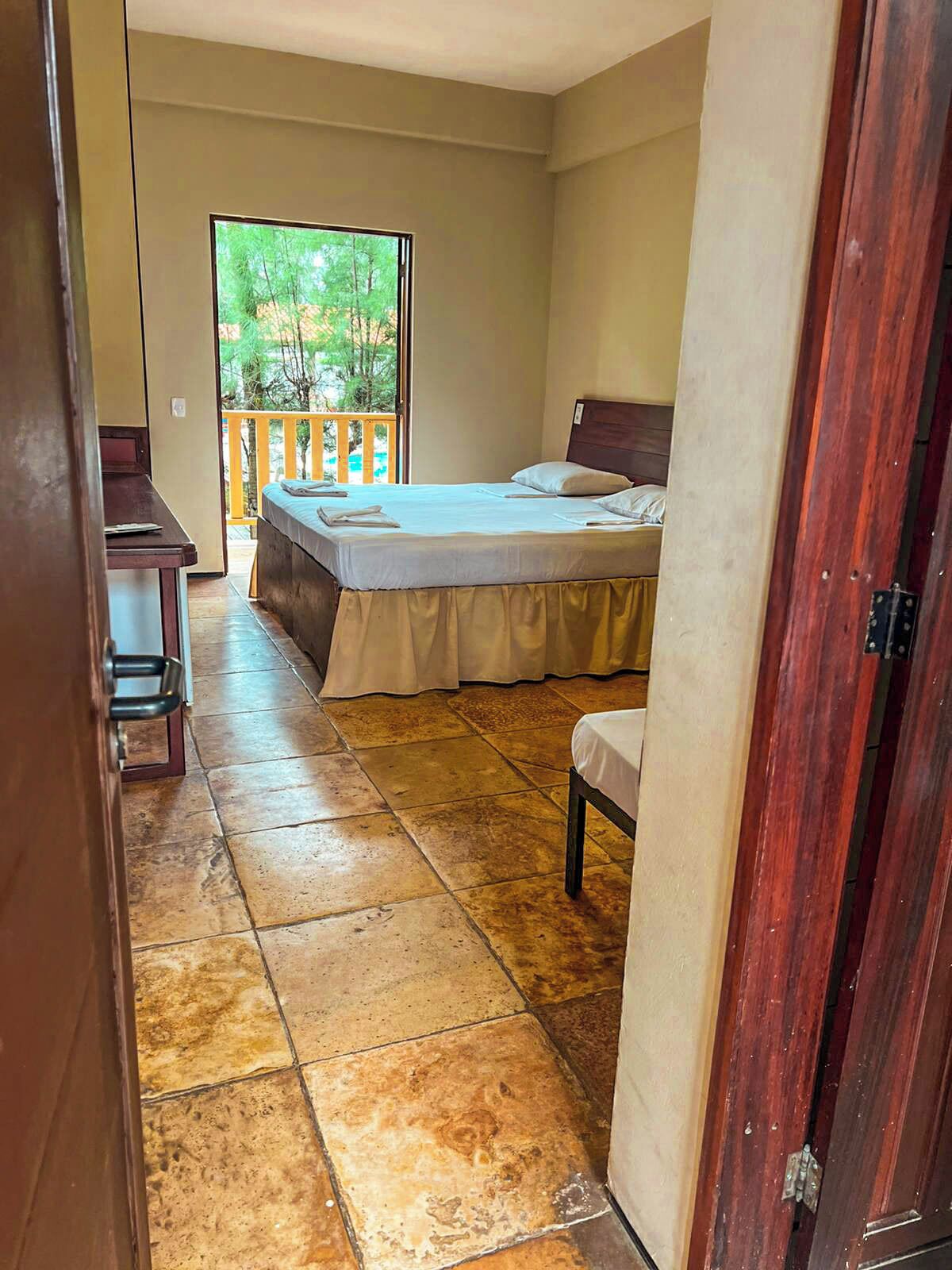 A bedroom with a bed, a chair, a desk, and a view of a balcony.