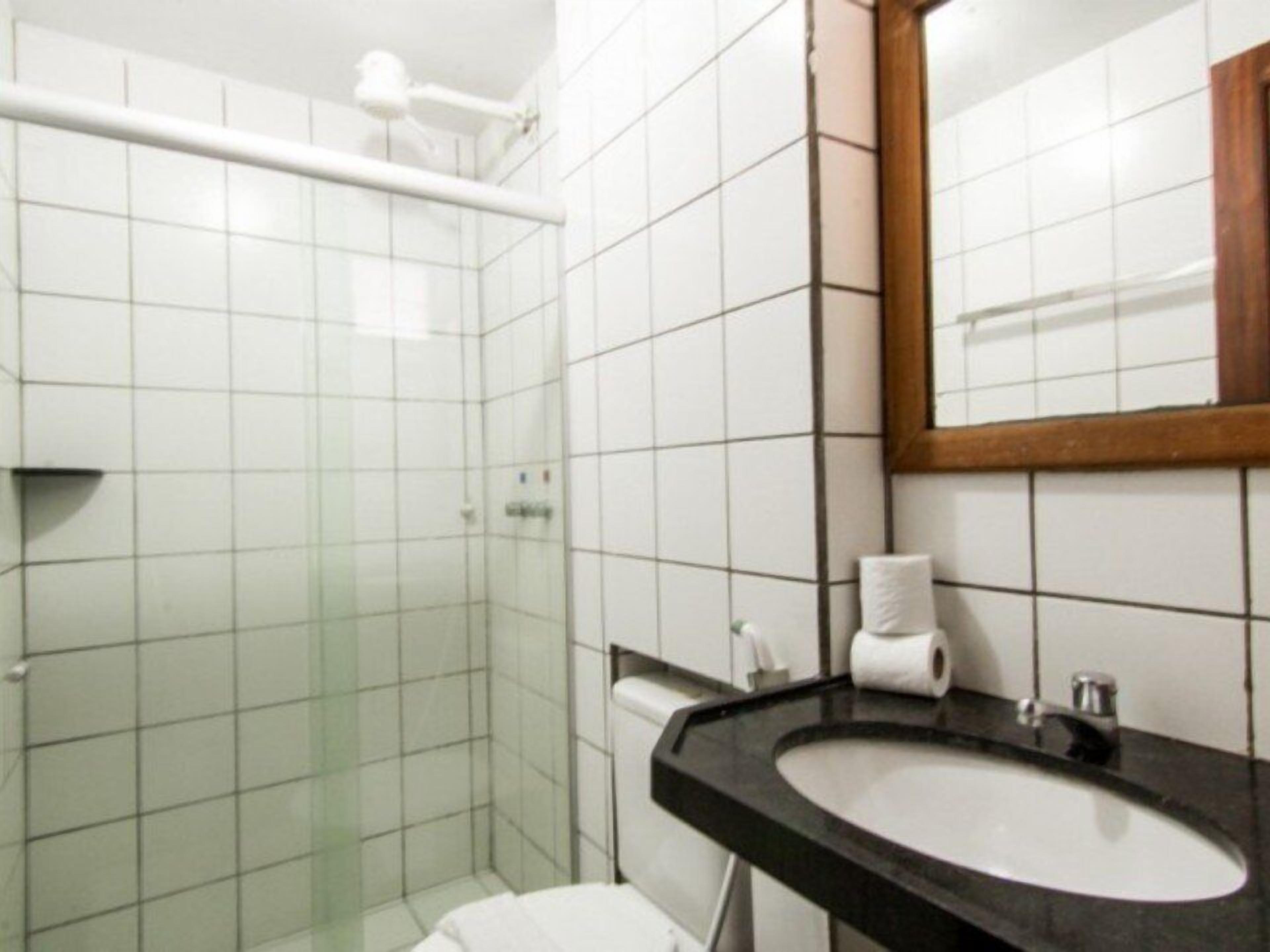 Un baño con azulejos blancos, un lavabo negro, un espejo y un inodoro.