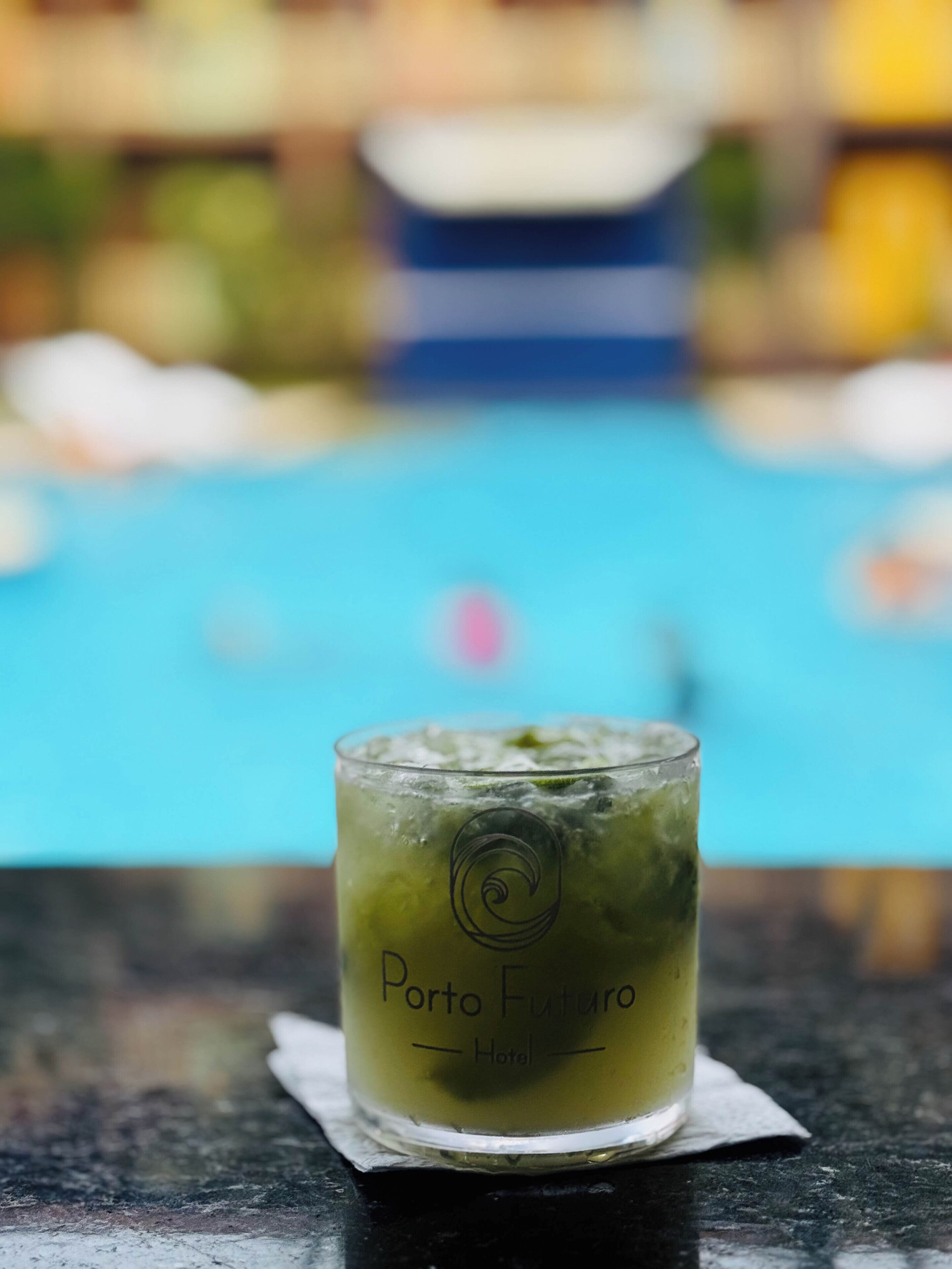 A glass with a green drink on a table near a pool.