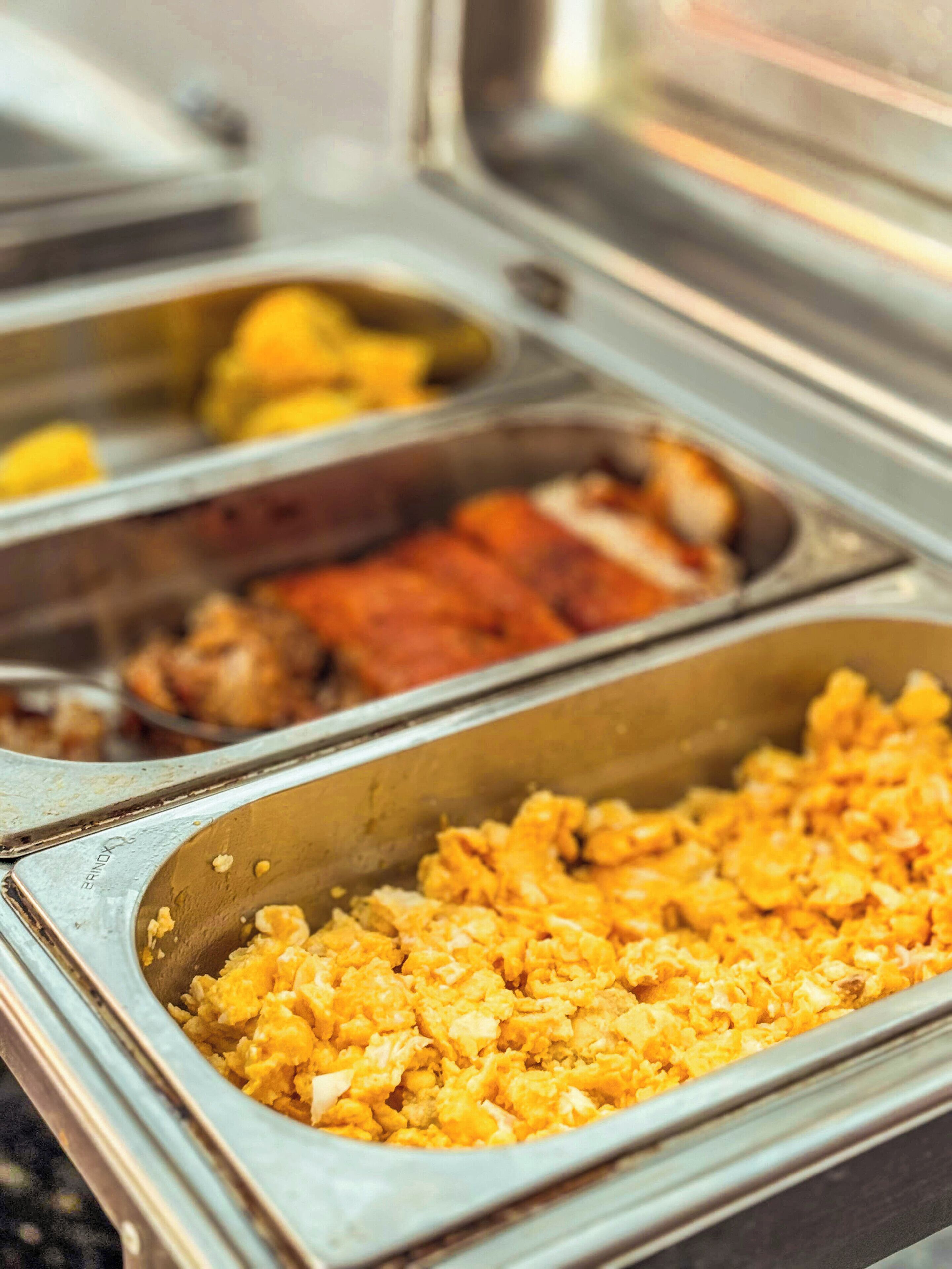 A buffet with various food items including scrambled eggs, salads, and meats.