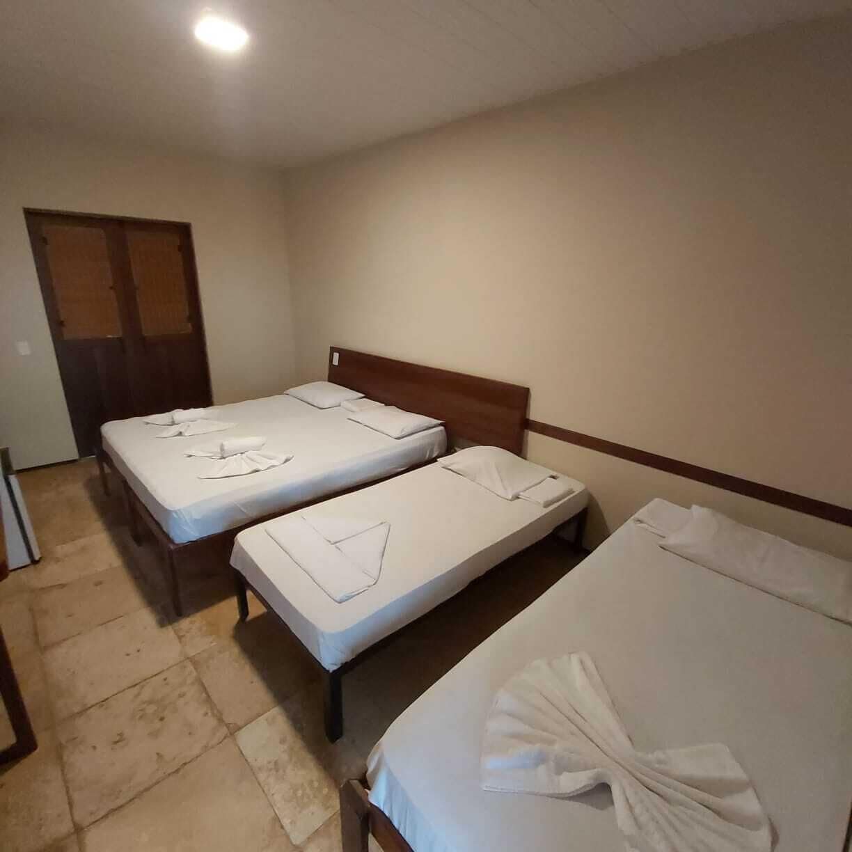 Habitación con tres camas individuales, cada una con ropa blanca y toallas.