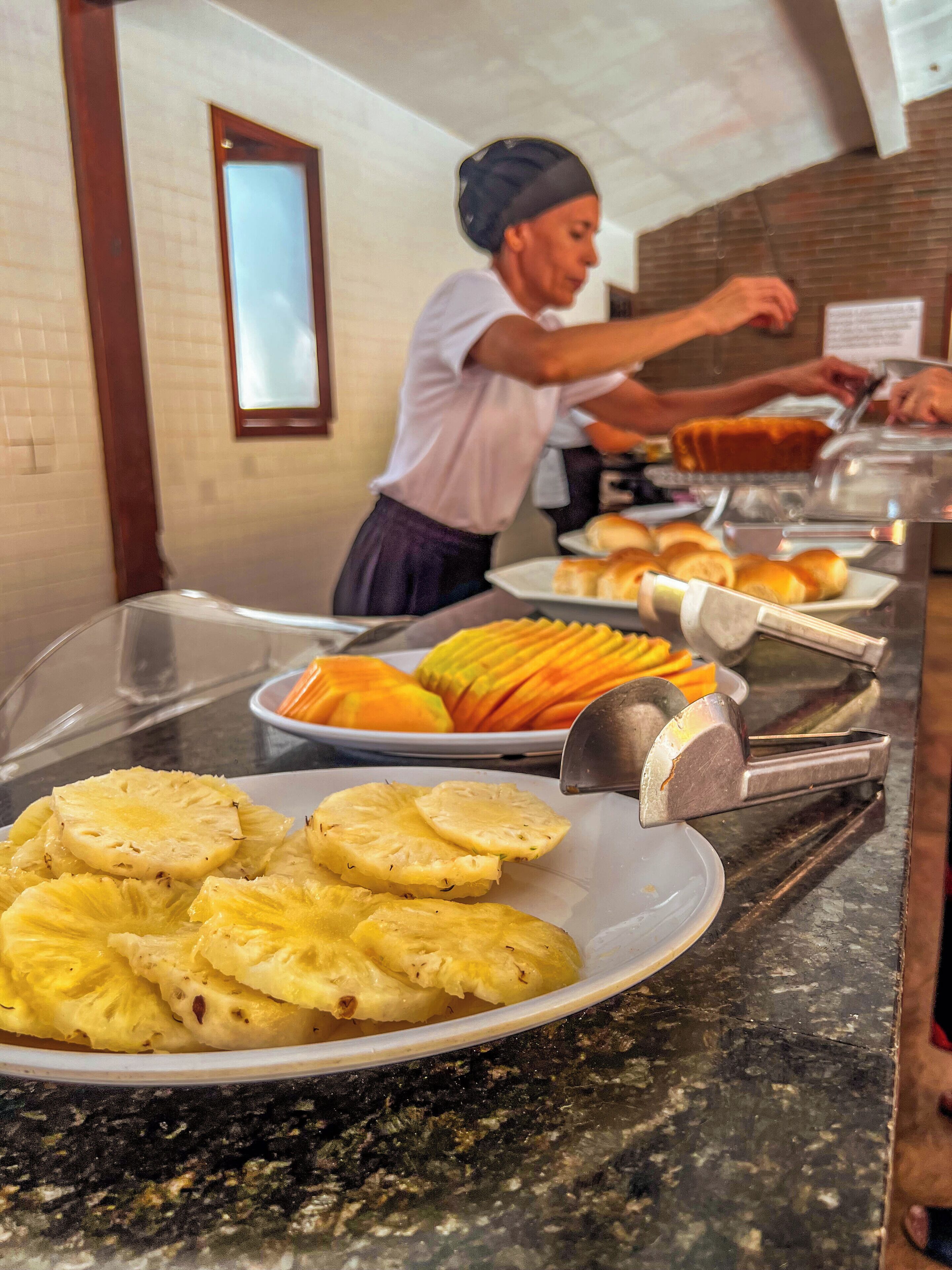 Buffet com diversos alimentos, incluindo fatias de abacaxi e um bolo.