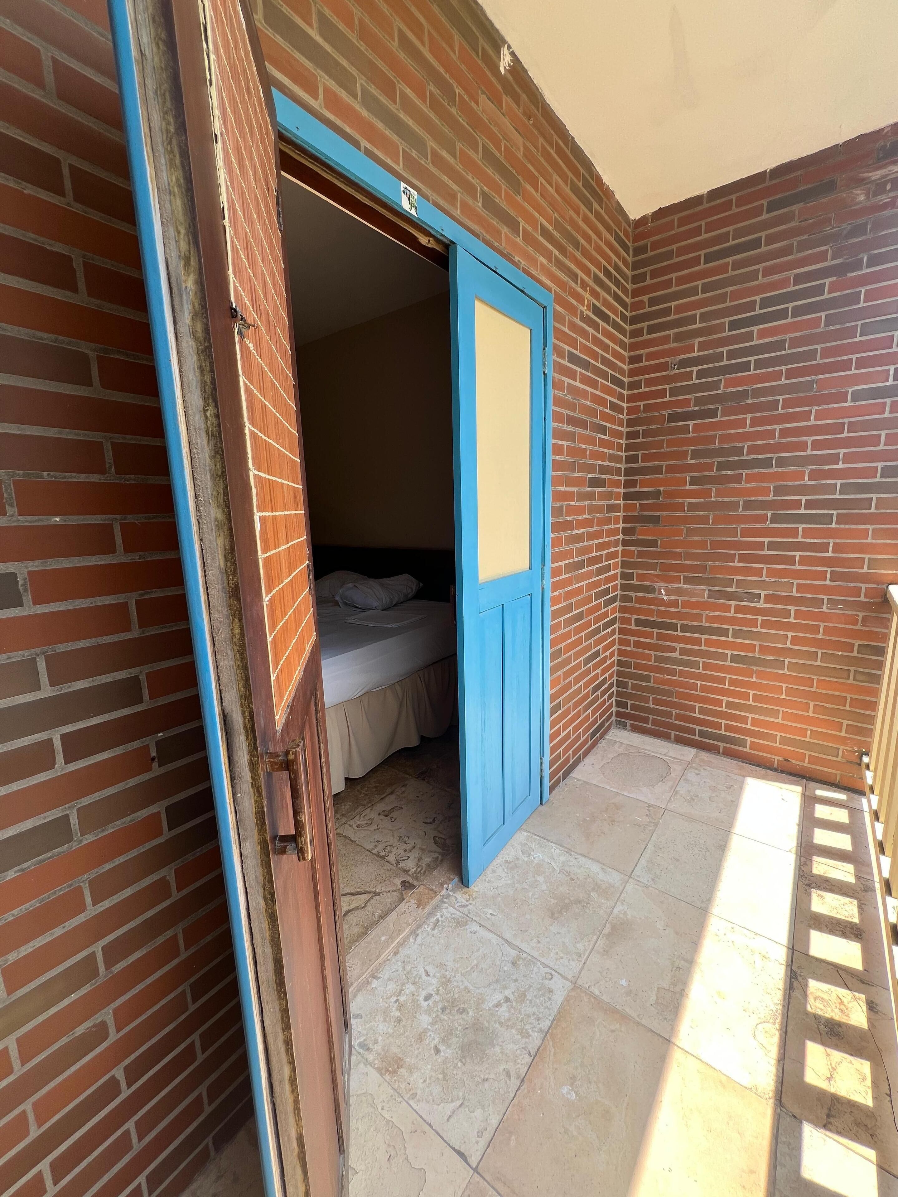 A room with a bed, a blue door, and a tiled floor.