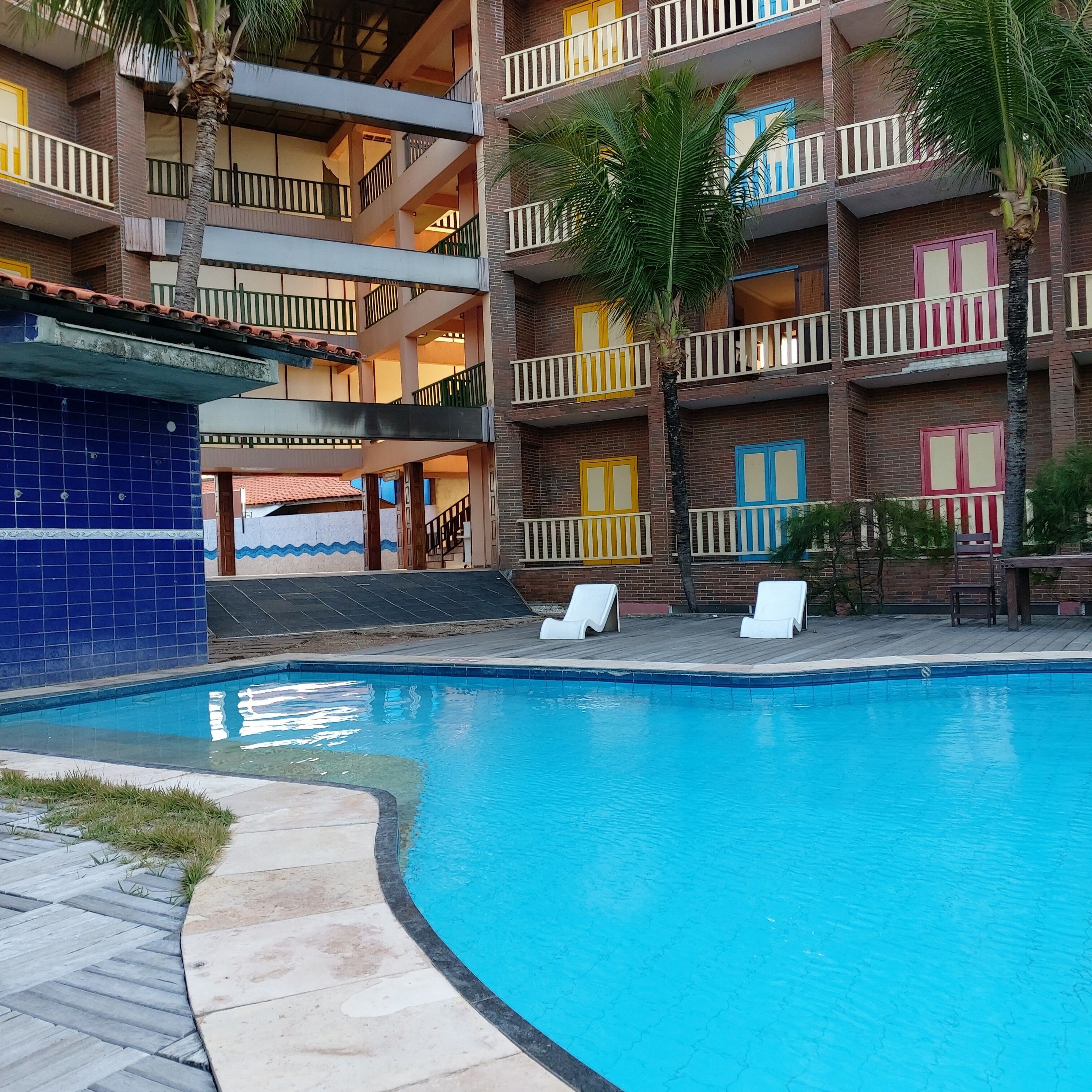 Un hotel de varios pisos con piscina, balcones con barandillas y una pared exterior de azulejos.