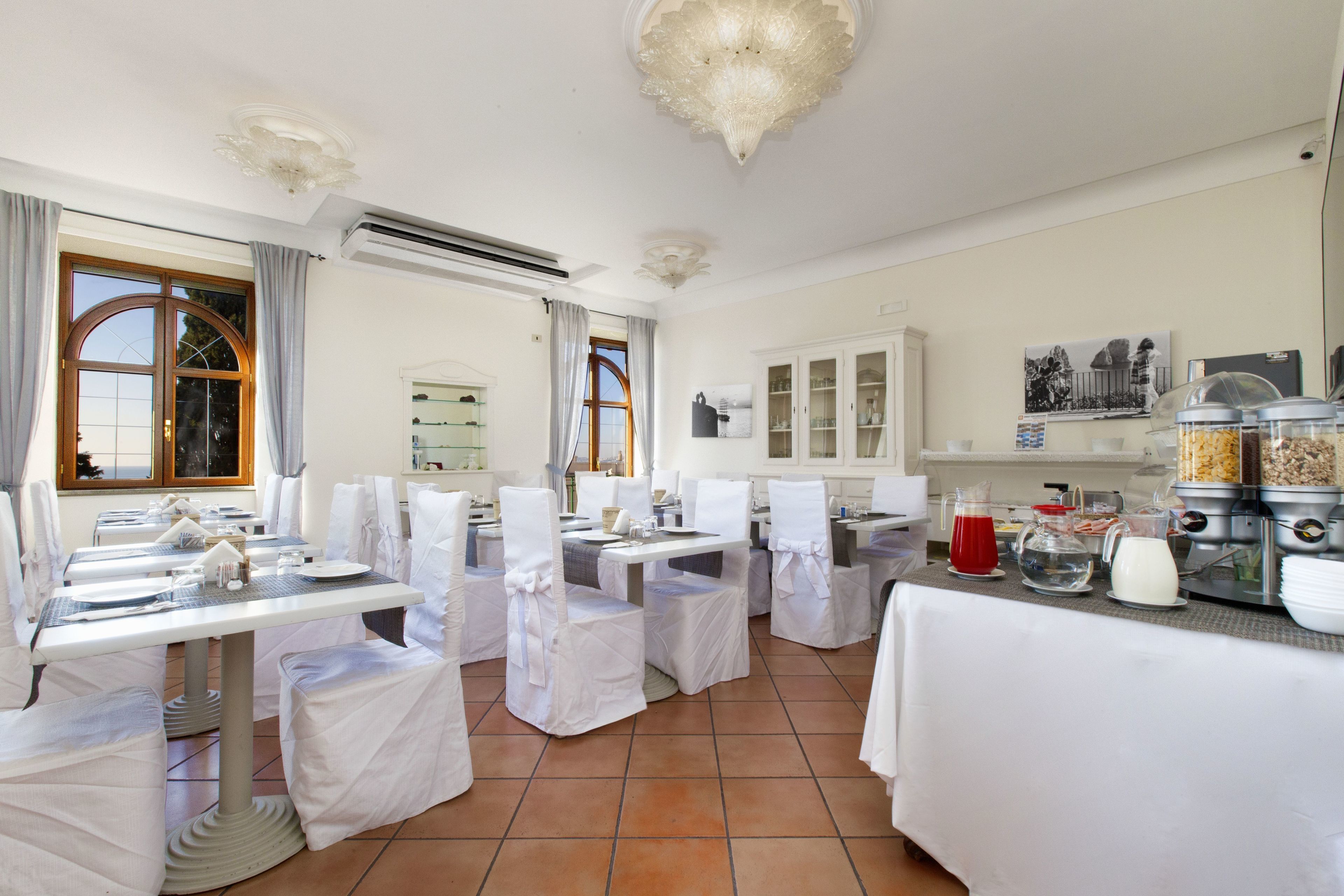 Zona de menjador amb taules preparades per a una refecció, cadires blanques i un aparador amb diferents aliments.