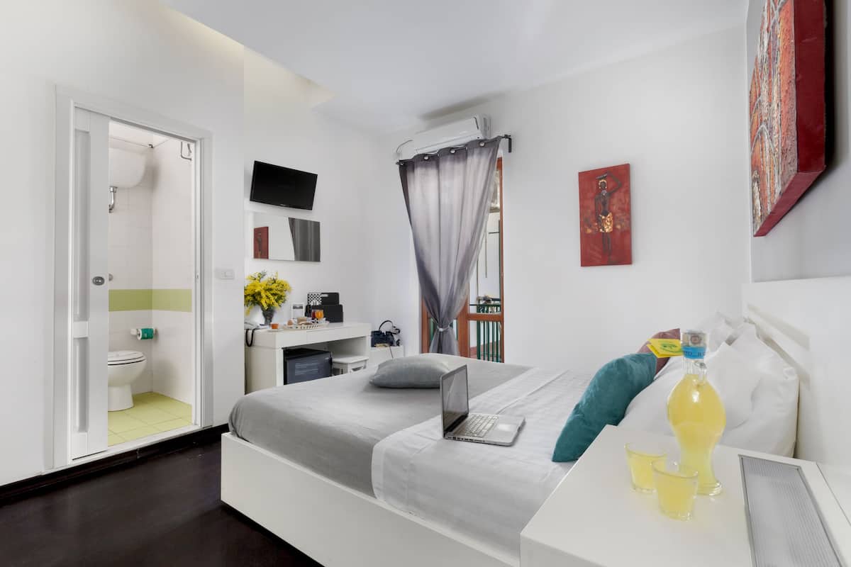 A modern bedroom with a bed, a desk, a laptop, a bottle of water, and a TV on the wall.