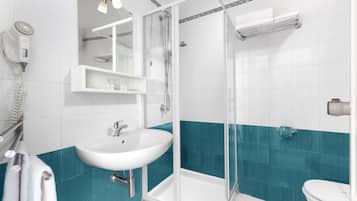 Un baño con lavamanos blanco, ducha con mampara de vidrio, inodoro y toallero.