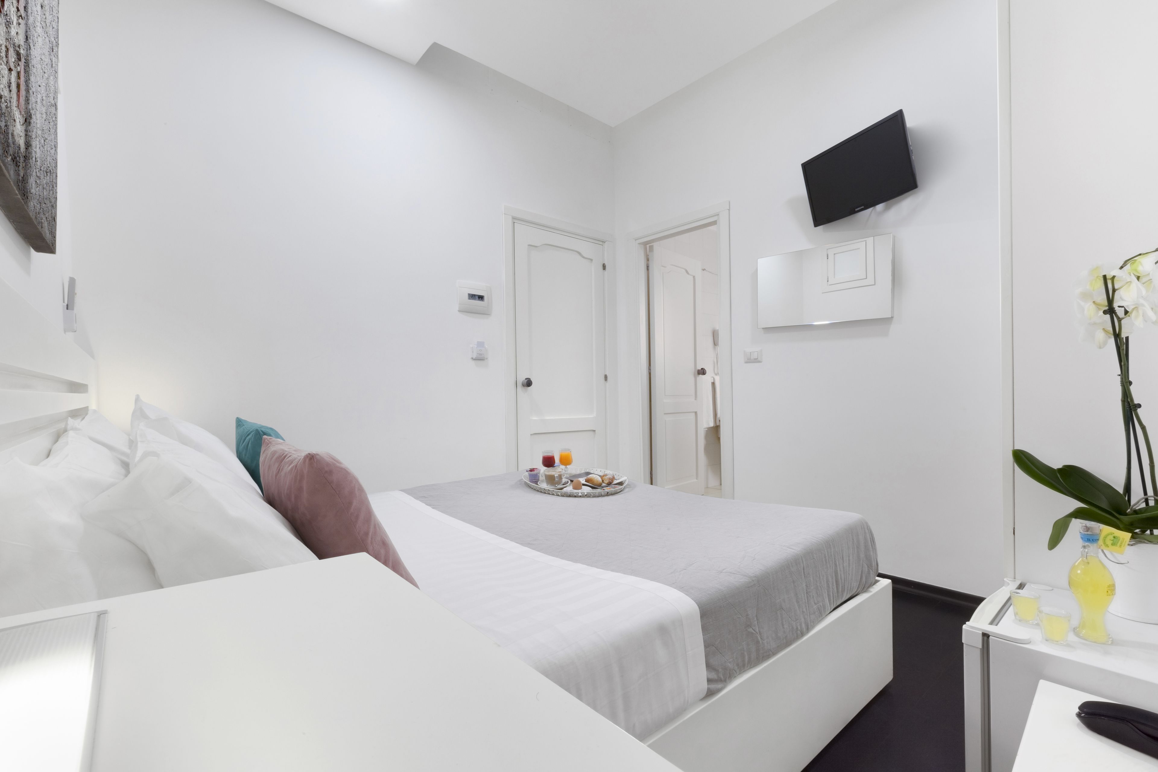 Moderni hotellihuone, jossa on sänky, yöpöytä ja seinälle asennettu televisio.