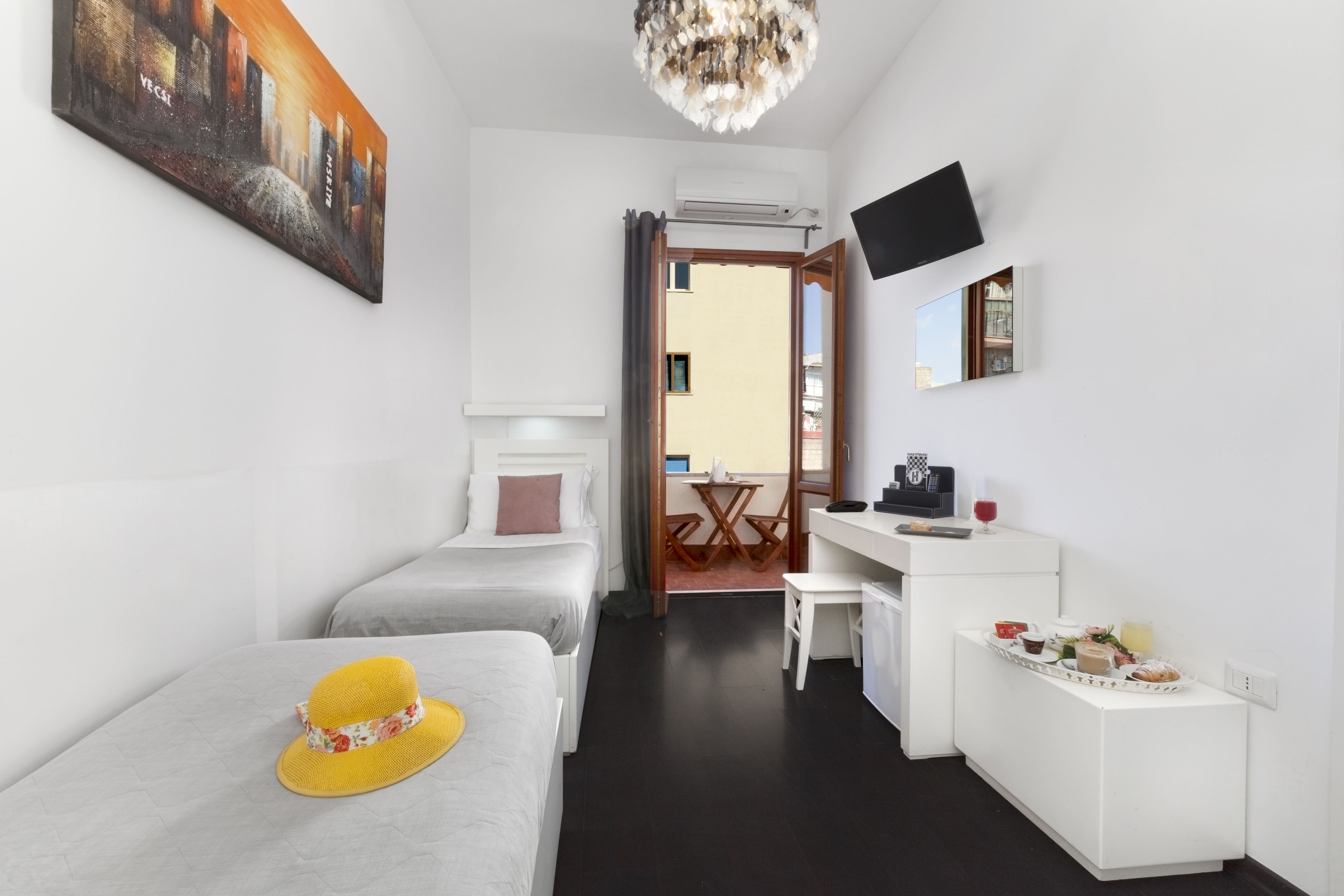 Habitación de hotel con cama, escritorio, silla, una pequeña mesa con comida y bebidas, televisión y un cuadro en la pared.