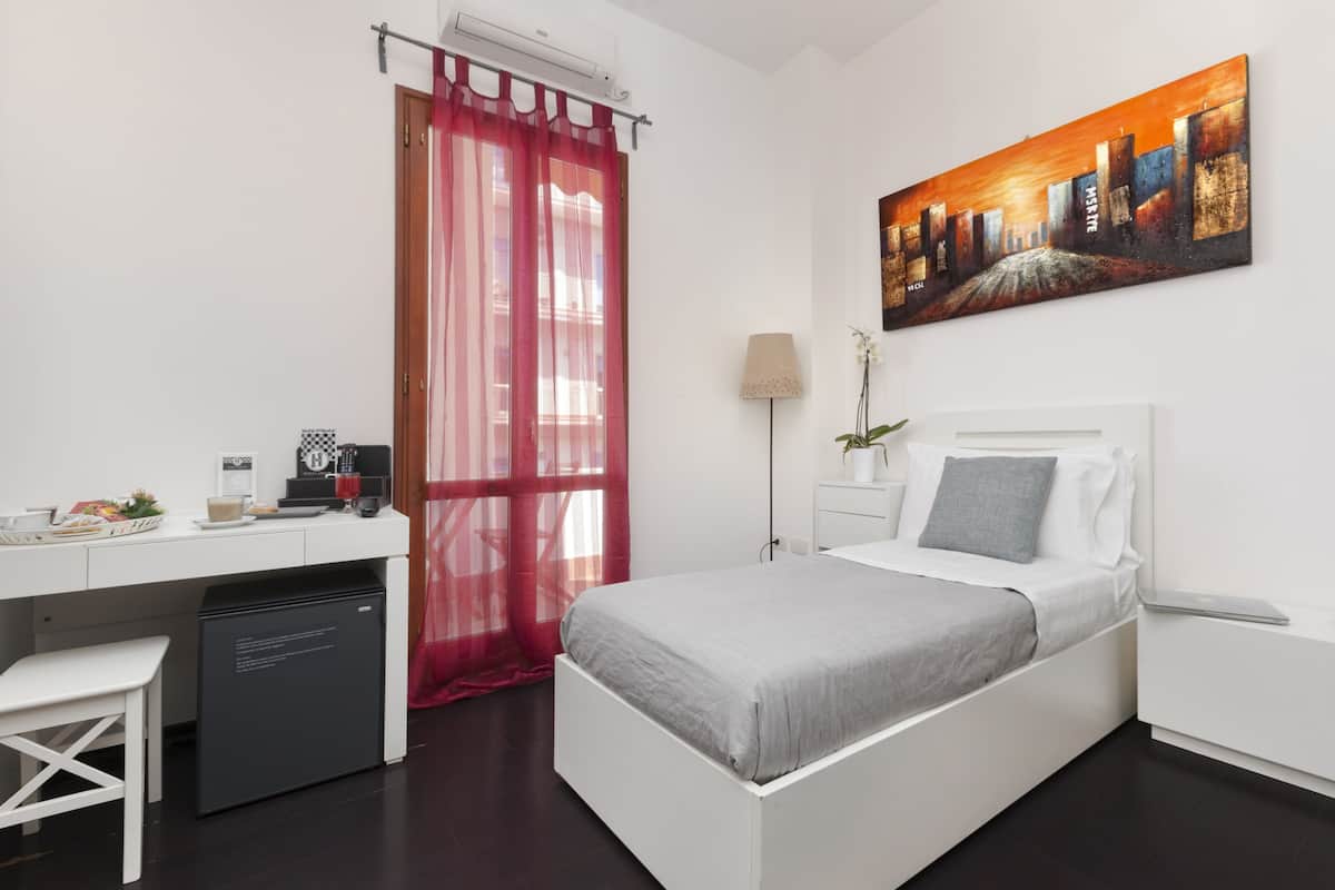 A modern bedroom with a white bed, a desk, a small white chair, a red curtain, and a painting on the wall.