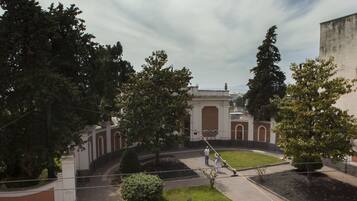 Une cour intérieure avec une fontaine centrale, entourée d’arbres et d’un bâtiment doté de fenêtres en arc de cercle.